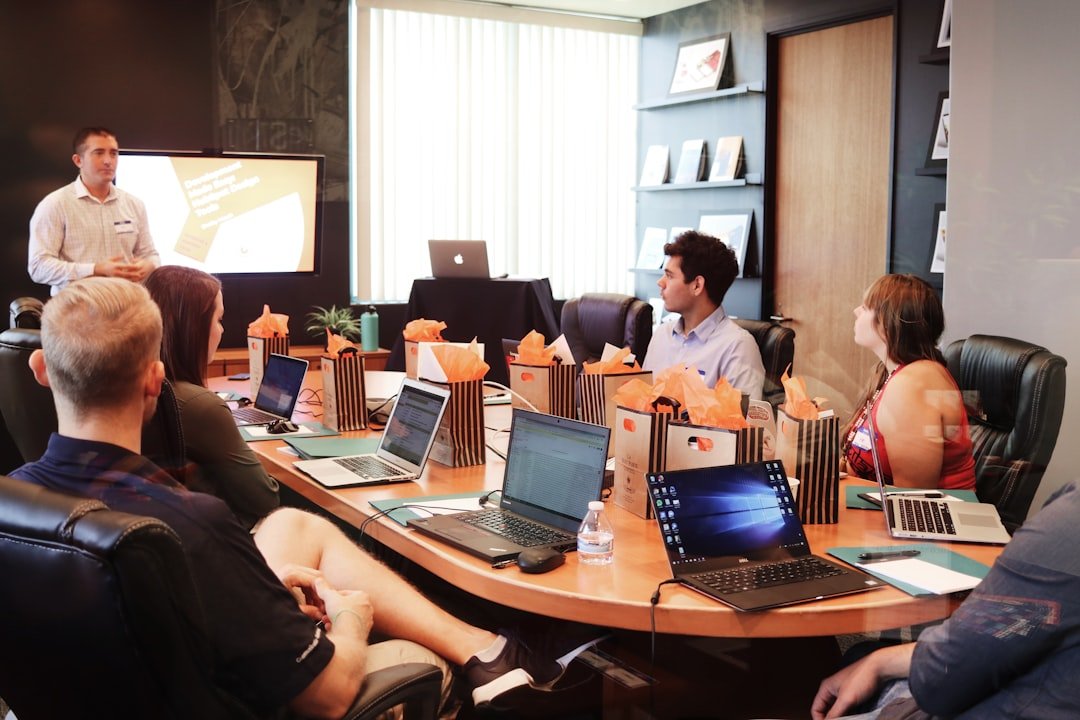 man-standing-in-front-of-people-sitting-beside-table-with-laptop-computers-gmsnxqiljp4